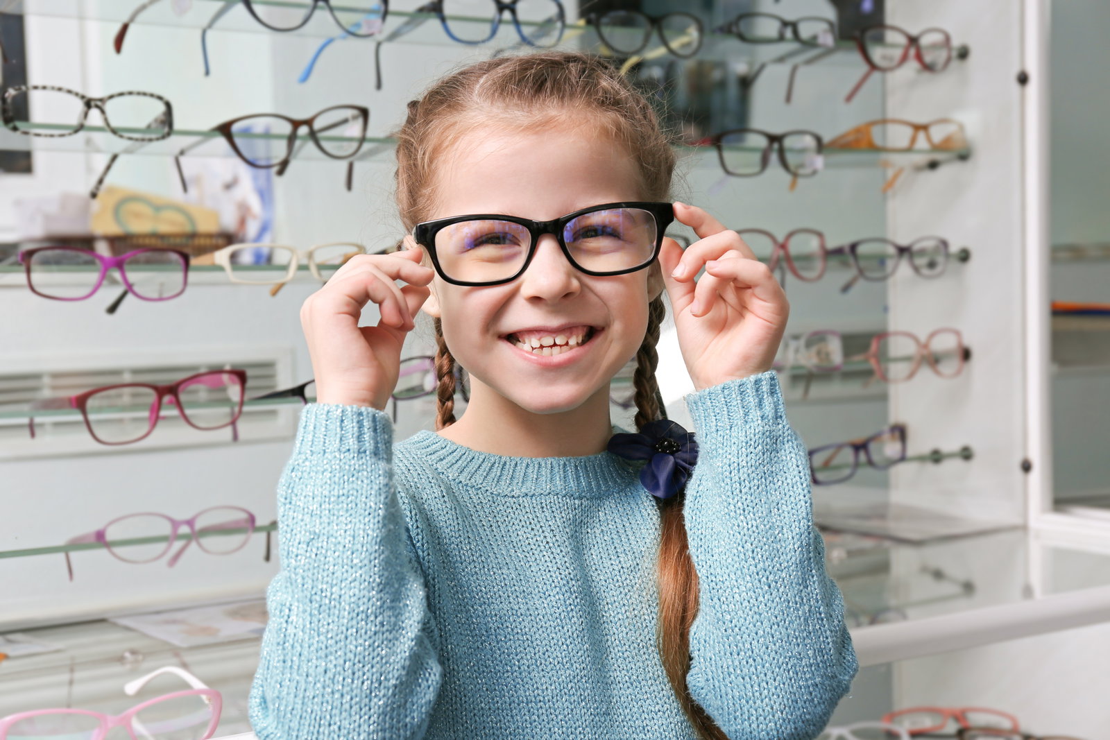 Das Bild zeigt ein lächelndes Mädchen mit einer Brille vor einer Brillenwand.